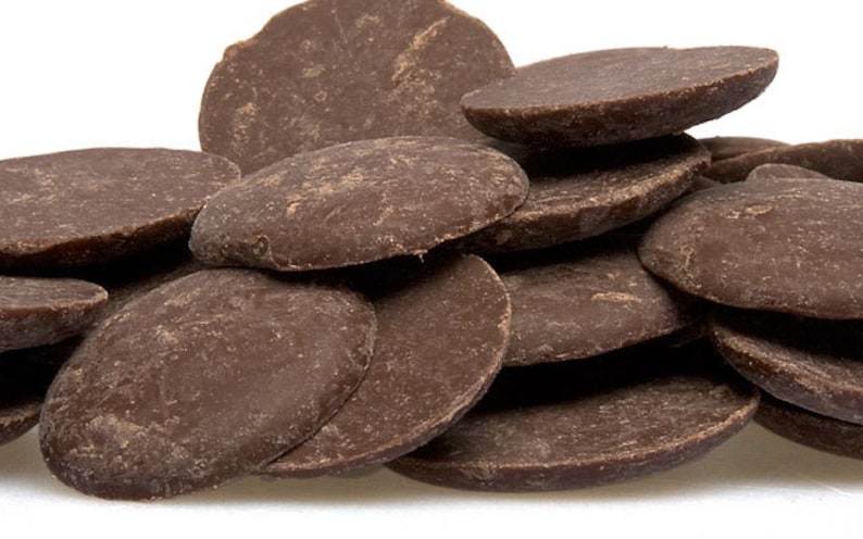 May include: A pile of dark brown chocolate discs, also known as chocolate chips, are stacked on top of each other. The chocolate discs are smooth and shiny.