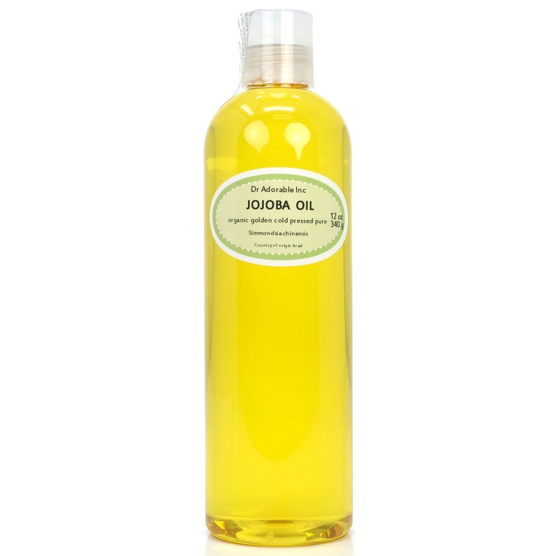 May include: A clear glass bottle filled with golden yellow jojoba oil. The label reads "Dr. Adorable Inc. JOJOBA OIL organic golden cold pressed pure 12 oz 340g Simmondsiachinensis Country of origin: Israel"