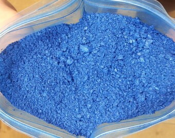 May include: A close-up view of a blue powder in a clear plastic bag. The powder is fine and has a slightly metallic sheen.