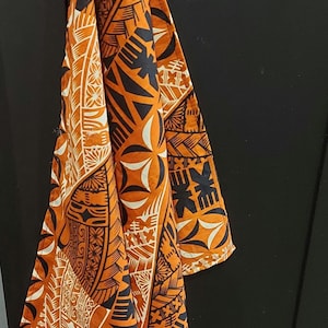 May include: A vibrant orange and black patterned fabric, featuring a geometric design. The fabric is displayed against a black background, highlighting the intricate patterns and colours. The design includes white and black shapes.