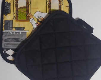 Puede incluir: Dos agarraderas de cocina. Una es negra y acolchada. La otra tiene un fondo amarillo con una ilustración de un chef y una escena de cocina. Las agarraderas están diseñadas para proteger las manos del calor.