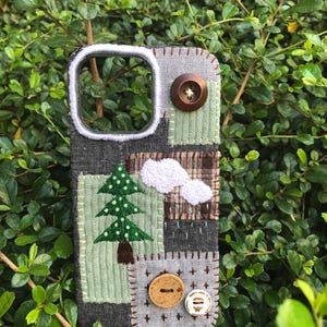 Könnte beinhalten: Eine rechteckige Handyhülle mit einem Patchwork-Design aus dunkelgrauem Denim, hellgrünem Cord und braunem Karostoff. Die Hülle ist mit einem gestickten grünen Tannenbaum, weißen Wolken, drei runden Knöpfen und weißen Ziernähten versehen.