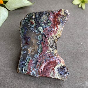 Puede incluir: Una piedra de forma irregular y colorida con una superficie pulida. La piedra presenta una mezcla de tonos rojos, verdes, azules y amarillos, con un centro cristalino translúcido. El aspecto general es natural y orgánico, lo que sugiere un objeto decorativo o de colección.