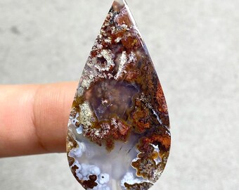 May include: A teardrop-shaped gemstone with a polished surface. The stone features a mix of colours, including brown, white, and purple, with intricate patterns resembling a landscape. The top of the stone is pointed, and the bottom is rounded.