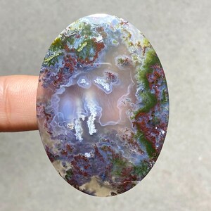 May include: Oval-shaped moss agate gemstone with a unique pattern. The stone features a blend of colors, including green, red, purple, and white, creating a natural, artistic design. The polished surface highlights the intricate details of the stone.