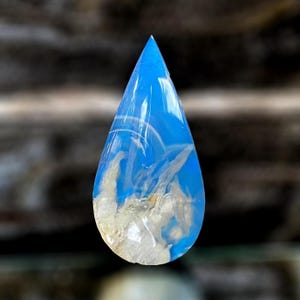 May include: A teardrop-shaped pendant with a vibrant blue hue, featuring white and cream-colored inclusions. The resin-cast piece has a pointed top and a rounded base, creating a unique and eye-catching design. The pendant is suitable for jewelry making.