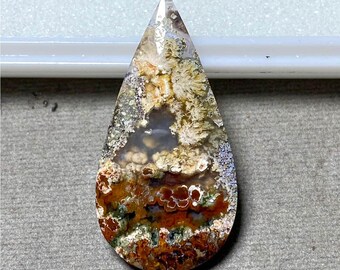 May include: A teardrop-shaped gemstone with a polished surface. The stone features a mix of colors, including brown, orange, white, and gray, with intricate patterns resembling a landscape. The top of the stone is pointed, and the bottom is rounded.