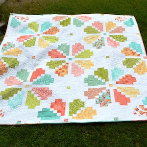 Könnte beinhalten: Eine weiße Steppdecke mit einem geometrischen Muster in Grün-, Rosa- und Gelbtönen. Die Steppdecke besteht aus Quadraten und Rechtecken, und das Muster erinnert an eine Blume.