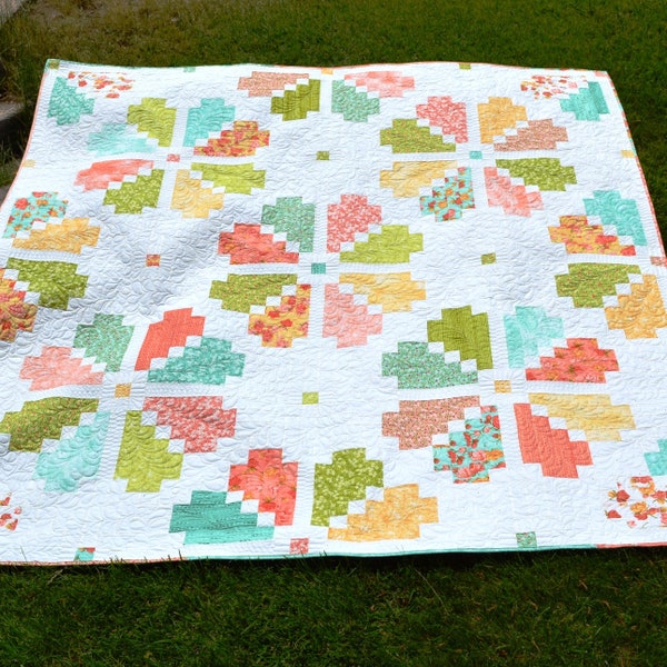 May include: A white quilt with a geometric pattern in shades of green, pink, and yellow. The quilt is made up of squares and rectangles, and the pattern is reminiscent of a flower.