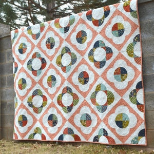 Puede incluir: Una colcha con fondo blanco y un patrón repetitivo de círculos rosas, verdes, azules y naranjas. Los círculos están rodeados por un diseño blanco festoneado.