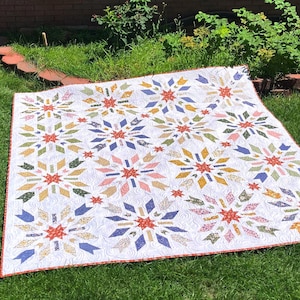 Puede incluir: Una colcha cuadrada con fondo blanco con un patrón de remolinos y múltiples motivos en forma de estrella en varios colores, incluidos rojo, azul, amarillo, verde y rosa. La colcha está terminada con un borde fino con un patrón rojo y blanco.