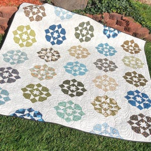 May include: A white quilt with a black border featuring a repeating pattern of geometric star shapes in shades of green, blue, and brown.