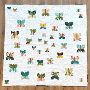 May include: A white quilt with a repeating pattern of green, pink, and yellow butterflies. The butterflies are arranged in a spiral pattern.