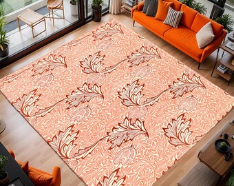 May include: A large, rectangular area rug with a repeating pattern of stylized leaves in shades of peach, cream, and brown. The rug is placed in a modern living room with an orange sofa and large windows overlooking a green landscape.