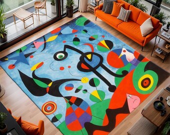 May include: A large, rectangular area rug with an abstract design in a living room setting. The rug features a blue background with colorful shapes, including red, yellow, green, and black. The room has an orange sofa and large windows.