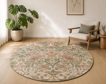 May include: A round area rug featuring a detailed botanical pattern with muted green leaves, soft pink flowers, and stylized birds. The intricate design covers the entire surface of the rug, which is laid flat on a light-colored wooden floor.