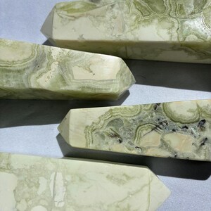 Puede incluir: Primer plano de varios obeliscos de cristal con dise&ntilde;os verdes y blancos. Los obeliscos tienen forma rectangular con una parte superior puntiaguda. La piedra tiene un aspecto veteado con remolinos verdes y blancos.