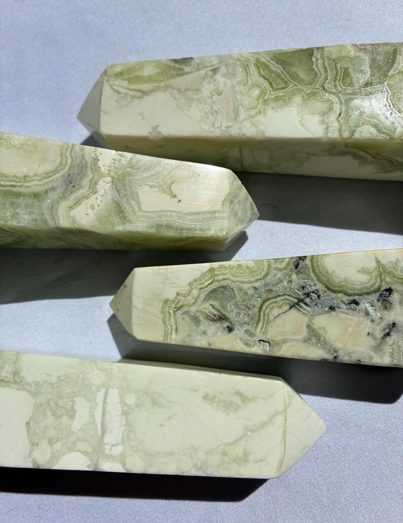 Puede incluir: Primer plano de varios obeliscos de cristal con dise&ntilde;os verdes y blancos. Los obeliscos tienen forma rectangular con una parte superior puntiaguda. La piedra tiene un aspecto veteado con remolinos verdes y blancos.