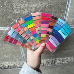 May include: A fan of colorful sticky notes in various shades of red, orange, yellow, green, blue, purple, and pink. The notes are arranged in a semi-circle shape.