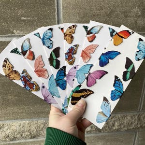May include: A set of colorful butterfly bookmarks with different designs and colors. The bookmarks are made of paper and have a glossy finish.