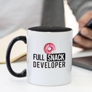 May include: White ceramic mug with a black rim and handle. The mug has a pink donut with a bite taken out of it and the text "FULL SNACK DEVELOPER" in black.