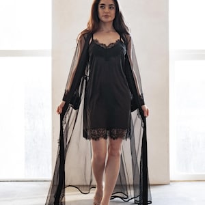 May include: A black lingerie set featuring a slip dress with lace trim and a sheer, dotted robe. The robe has long sleeves and lace detailing. The set is designed for sleepwear or loungewear.
