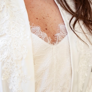 May include: White satin robe with delicate lace detailing. The robe features a V-neckline and long sleeves.