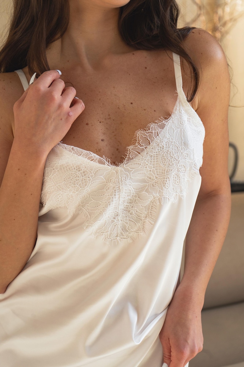 May include: A white satin slip dress with delicate lace trim around the neckline.