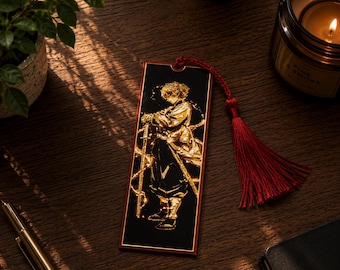 Puede incluir: Marcapáginas rectangular con una ilustración dorada de un personaje con una espada sobre fondo negro. Tiene una borla roja. La ilustración tiene detalles dorados. Es un artículo decorativo.