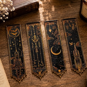 Könnte beinhalten: Vier schwarz-goldene Lesezeichen mit himmlischen und gotischen Designs. Jedes Lesezeichen zeigt eine andere Illustration, darunter eine Fledermaus, ein Schloss, ein Halbmond und eine Kirche. Die Lesezeichen sind rechteckig mit dekorativem Rand.