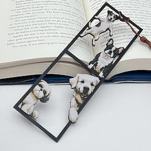 May include: A black rectangular bookmark featuring illustrations of four different dog breeds. The dogs are a Jack Russell Terrier, a French Bulldog, a Golden Retriever, and a Shih Tzu. The bookmark has a brown tassel.