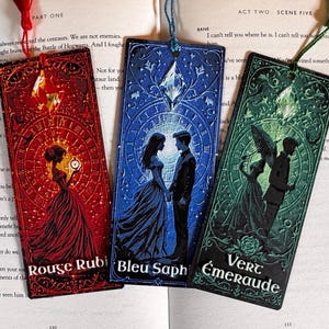 May include: Three decorative bookmarks with romantic illustrations in red, blue, and green. Each bookmark features a unique design and the text "Rouge Rubi", "Bleu Saph", and "Vert Émeraude". Each bookmark has a tassel attached at the top.