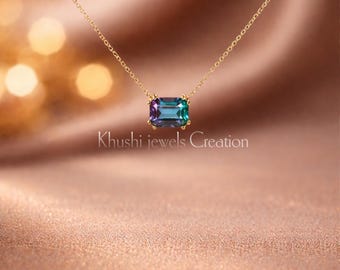 Puede incluir: Un collar de oro con un colgante rectangular de piedra preciosa que cambia de color. El colgante cambia de morado a turquesa. El collar se muestra sobre un fondo de satén. El texto de la imagen dice "Khushi jewels Creation."