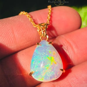 Può includere: Una collana con catena d'oro con un ciondolo a forma di pera in opale. L'opale è iridescente con sfumature di blu, verde e giallo.
