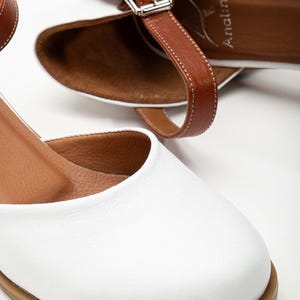 May include: White leather sandals with brown leather straps and buckle closures. The sandals have a rounded toe and a low heel. The brand name "Analin" is visible on the insole. The shoes are designed for everyday wear.