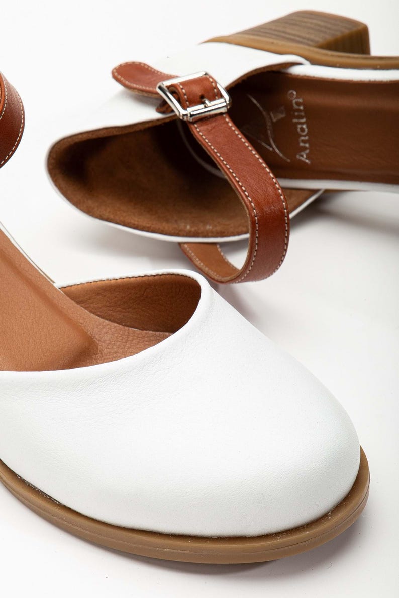 May include: White leather sandals with brown leather straps and buckle closures. The sandals have a rounded toe and a low heel. The brand name "Analin" is visible on the insole. The shoes are designed for everyday wear.