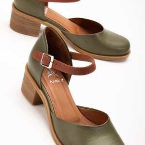 May include: Olive green leather Mary Jane style shoes with a brown ankle strap and a wooden block heel. The shoes have a rounded toe and a buckle closure. The brand name "Anali" is visible on the insole.
