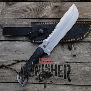 May include: A large, silver-bladed knife with a serrated edge and black handle, resting in a black leather sheath with yellow stitching. The knife has the text "M4X" and a skull logo. The word "PUNISHER" is printed below the knife.