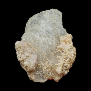 Può includere: Primo piano di un campione di minerale di colore chiaro su sfondo nero. Il minerale ha una struttura cristallina traslucida con aree beige e bianco sporco, che mostra una superficie ruvida e strutturata. La forma generale è irregolare e organica.
