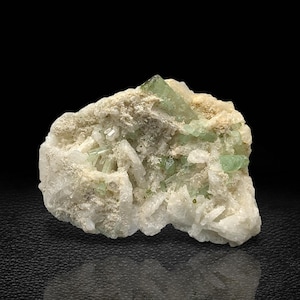 May include: A cluster of green crystals embedded in a white matrix. The crystals are translucent and have a glassy luster. The matrix is rough and textured.