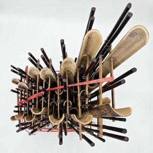 May include: A traditional musical instrument constructed from multiple vertical bamboo tubes of varying lengths, held together by thin wooden crossbars and secured with red elastic bands. The bamboo features natural tan and dark brown tones.
