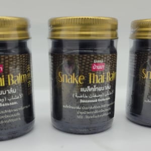 Può includere: Tre vasetti di Snake Thai Balm con coperchi dorati ed etichette nere. Le etichette presentano testo in più lingue, tra cui inglese e tailandese. I vasetti sono riempiti con una sostanza scura.