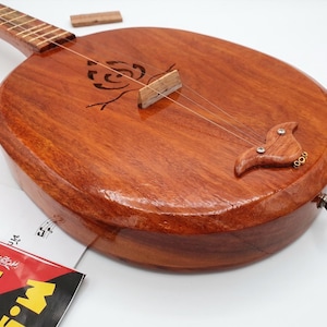 Może przedstawiać: Drewniany instrument strunowy z okrągłym korpusem i długą szyjką. Instrument ma ciepły brązowy kolor i dekoracyjny kwiatowy wzór. Posiada struny i kołki do strojenia.