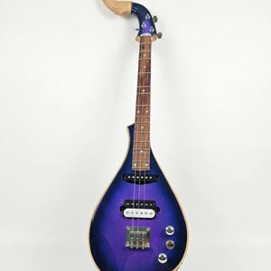 May include: A distinctive stringed instrument with a teardrop-shaped body, showcasing a purple and blue gradient. The neck is brown, and the headstock is decorated with a carved wooden dragon. Silver knobs and a bridge complete the design.
