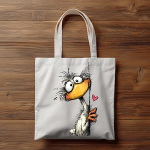 May include: White canvas tote bag featuring a whimsical cartoon duck with a large yellow beak, expressive eyes, and a red heart. The duck is drawn in a playful style, peeking from behind a line. The bag has two white handles.