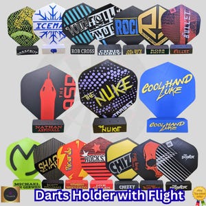May include: A collection of dart flights in various designs and colors, each mounted on a black holder. The flights feature graphics, text, and logos, including "ICEMAT", "VOLTA", "ROCK", and "THE NUKE". The text "Darts Holder with Flight" is at the bottom.