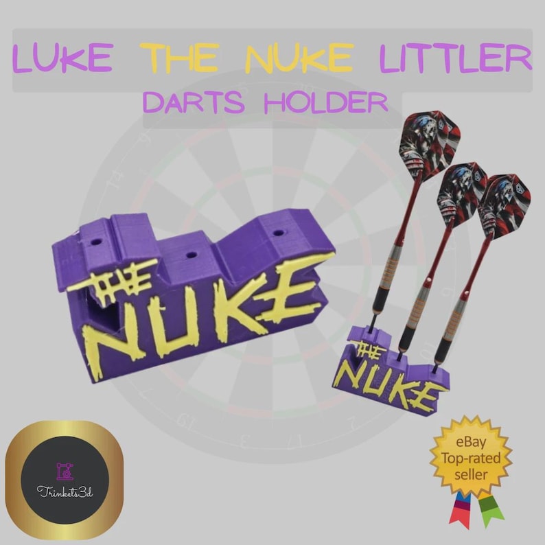 May include: A purple and yellow darts holder with the text "THE NUKE" and "LUKE THE NUKE LITTLER DARTS HOLDER". The image also shows three darts with red shafts and a graphic design on the flights.