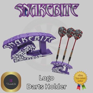 May include: Purple "Snakebite" logo darts holder with three darts. The holder has a snake design and the text "Snakebite". The darts have red shafts and patterned flights. The image also includes the text "Logo Darts Holder".
