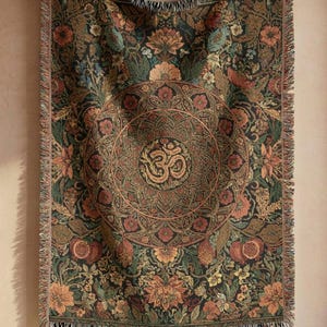 May include: A tapestry with a floral design in shades of green, brown, and orange, featuring a central circular pattern with the Om symbol. The tapestry has a fringed edge and is hanging on a wooden rod.