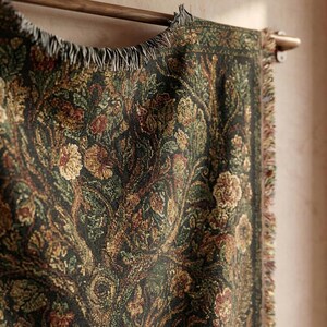 May include: A dark green tapestry with a floral pattern in shades of brown, gold, and red. The tapestry is hanging on a wooden rod and has a fringed edge. The design features stylized flowers and foliage.